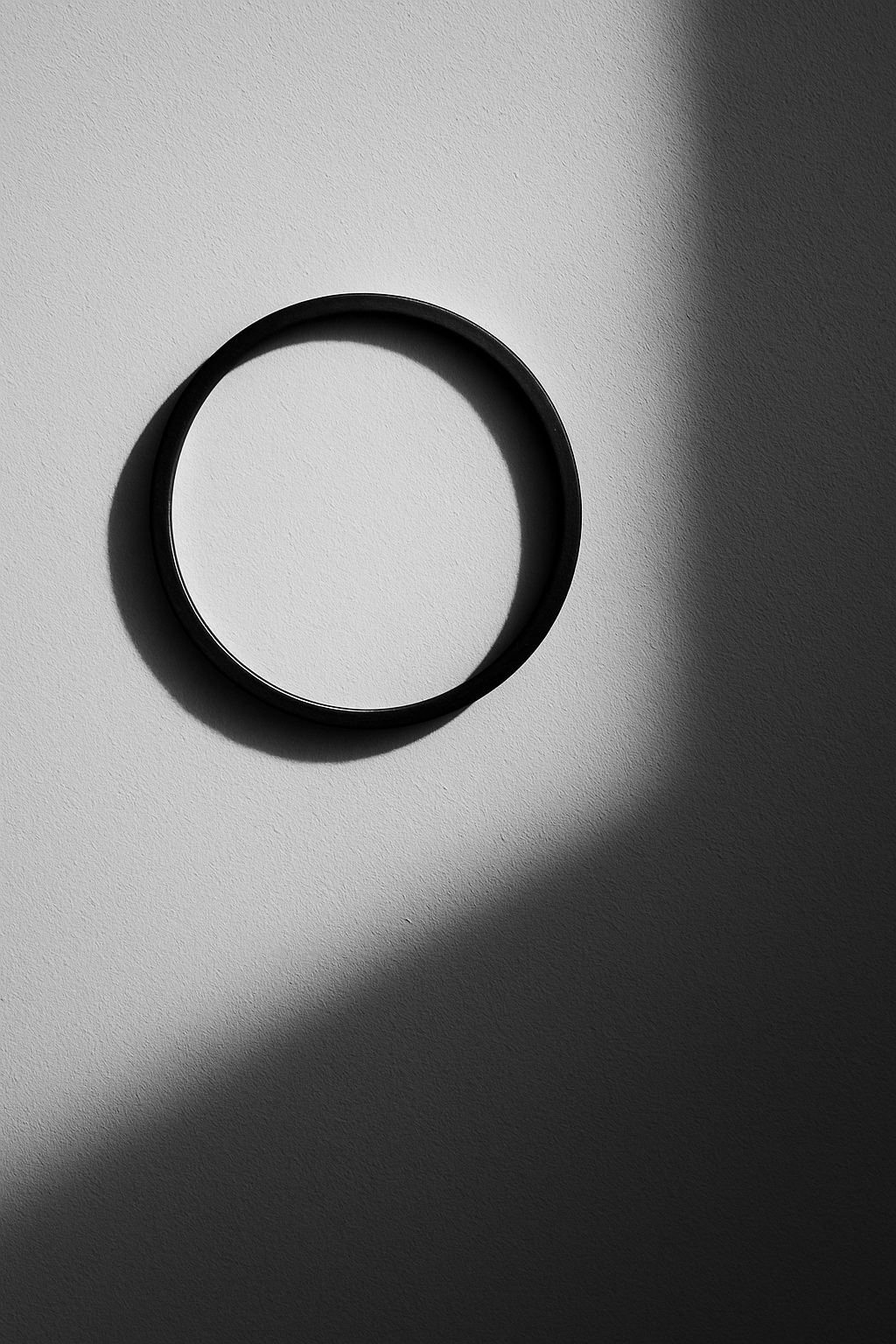 Schwarz-weiss Fotografie einer runden Uhr an einer hellen Wand, ohne Zeiger. Ein diagonal einfallender Schatten teilt die Fläche in hell und dunkel. Minimalistisch, ruhig, modern.